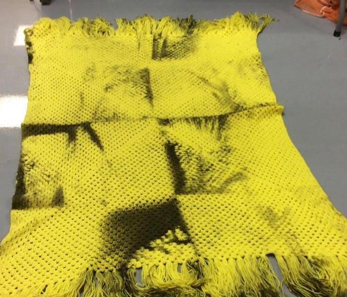 Yellow blanket with soot stains all over it from fire damage.